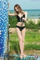 A woman in a black bathing suit standing next to a blue and white tiled wall.