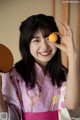 A woman in a pink kimono holding an orange in her hand.